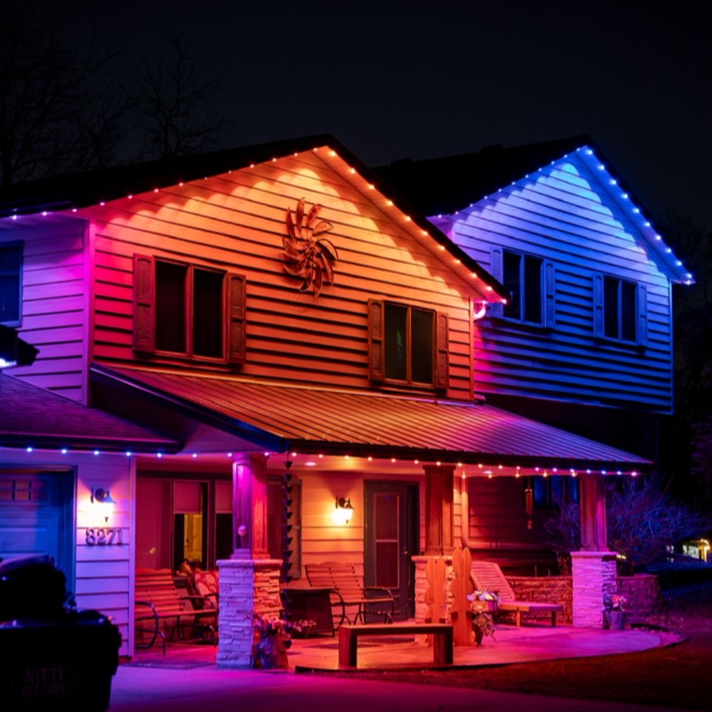 A two-story home glowing with red, blue, and pink holiday LED scenes after dark