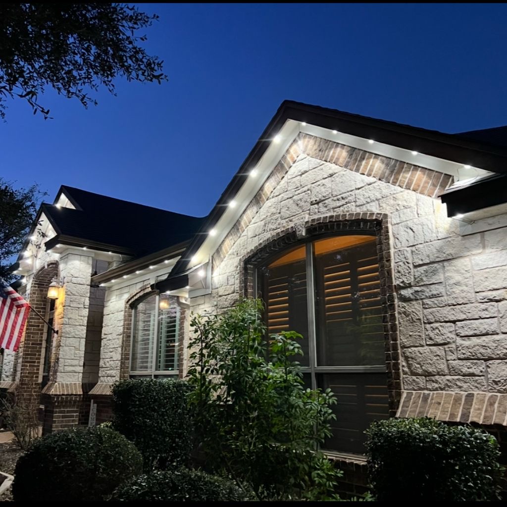 Warm white permanent LED lights outlining the gables and rooflines of a stone and brick home at dusk
